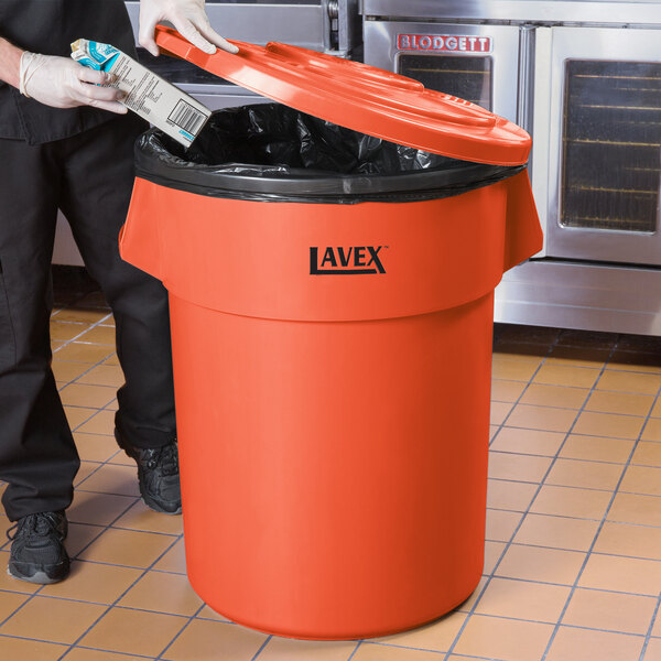 A man in a black apron putting a milk carton in a red Lavex garbage can.