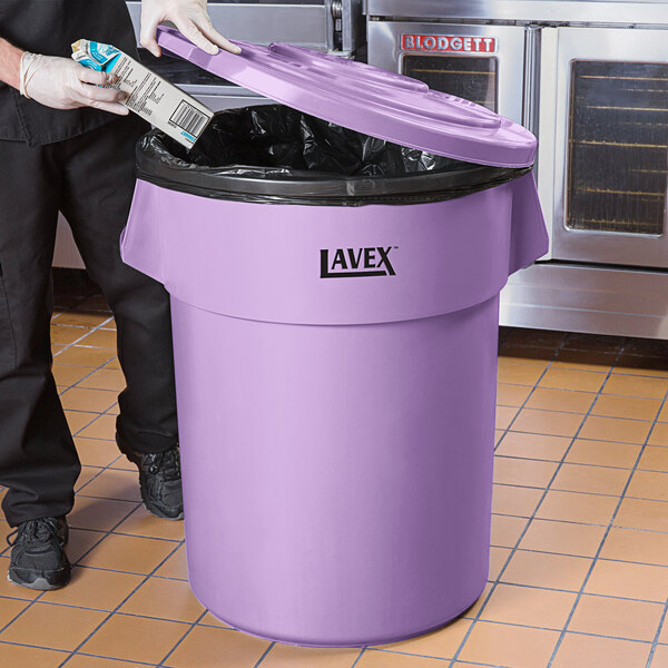 A man in a chef's uniform putting a carton in a Lavex purple trash can.