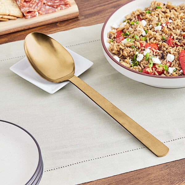 A spoon with a hammered gold handle next to a bowl of rice and vegetables.