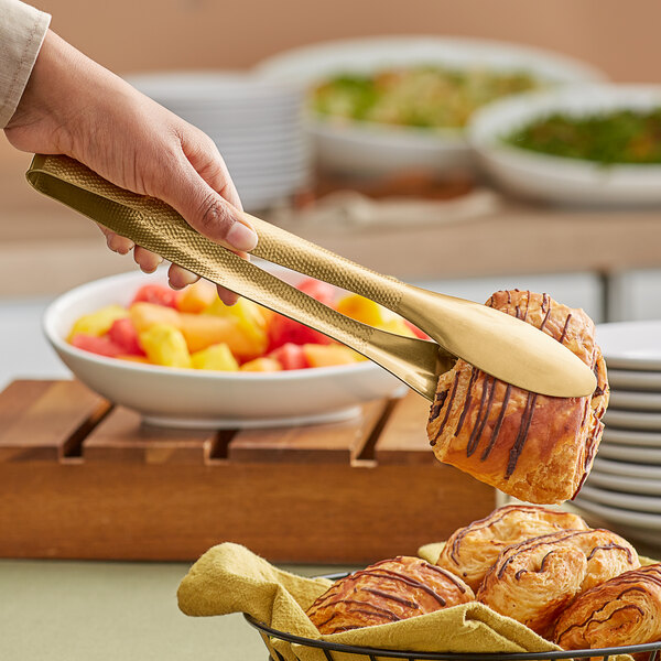 A hand using American Metalcraft hammered gold tongs to hold a pastry.