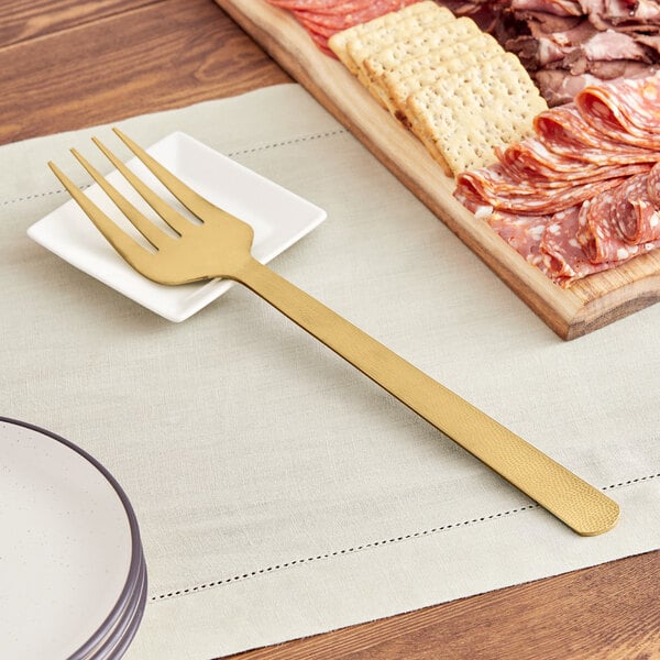 An American Metalcraft hammered gold cold meat fork on a plate of meat.