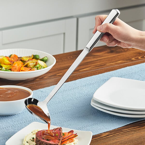 A person using an American Metalcraft stainless steel spout ladle to pour sauce on a bowl of food.