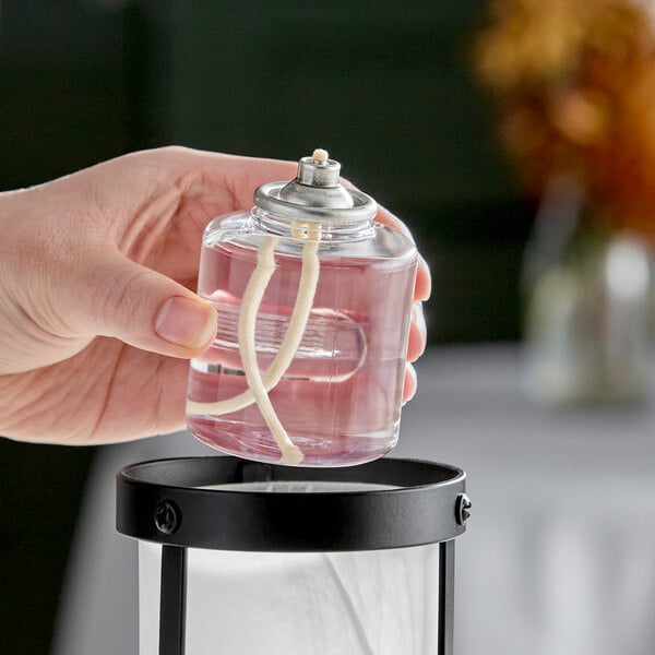 A clear liquid candle fuel cartridge with a visible wick being placed into a lantern.