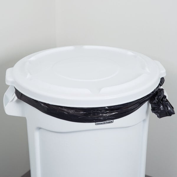 A white Rubbermaid BRUTE trash can lid on a white table over a black trash bag.