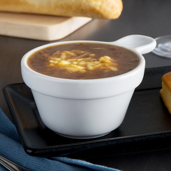 A Tuxton porcelain white china soup cup filled with soup on a table with bread and a knife.