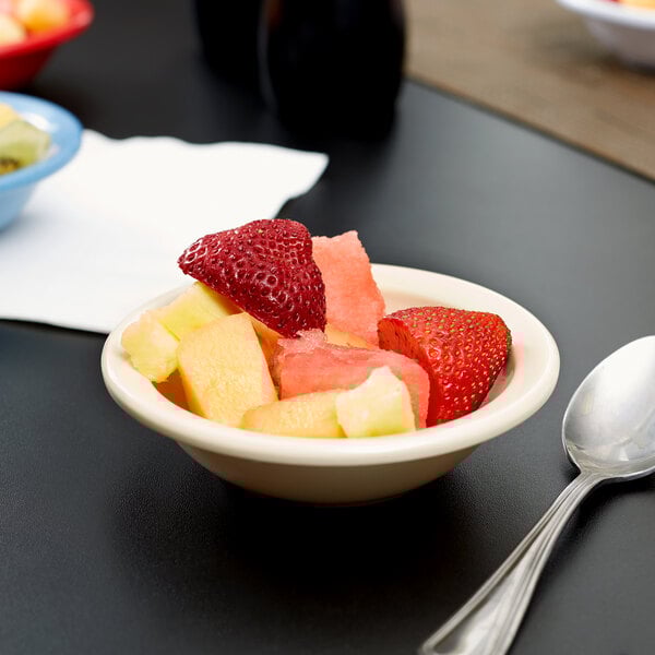 A Carlisle tan melamine fruit bowl filled with strawberries on a table with a spoon.