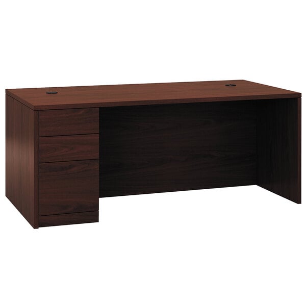 A brown mahogany laminate HON pedestal desk with drawers on it.