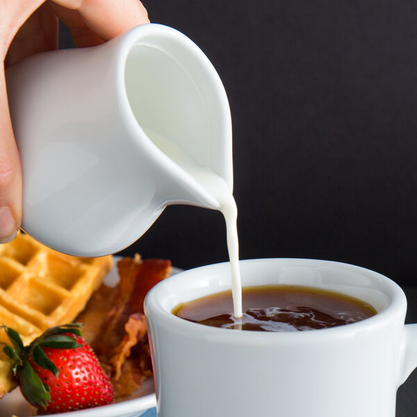 A person pouring milk into a cup of coffee.