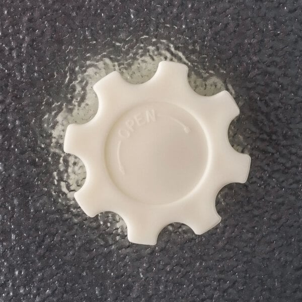 A white plastic gear-shaped freezer door knob with the word 'OPEN' and an arrow, attached to a textured gray surface.