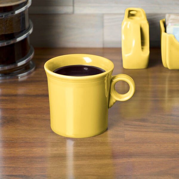 A yellow Fiesta china mug with a handle on a wooden surface.