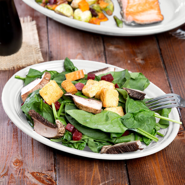 A Fiesta white china oval platter with salad and a fork on a table.