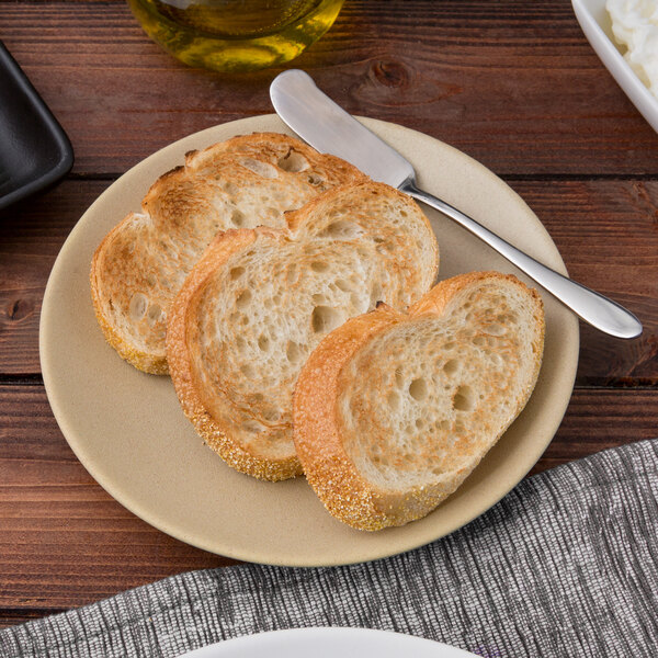 A Tuxton TuxTrendz matte beige coupe plate with a piece of bread on it.