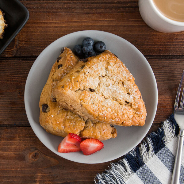 A TuxTrendz Zion matte gray coupe china bread and butter plate with pastries and strawberries on a table.