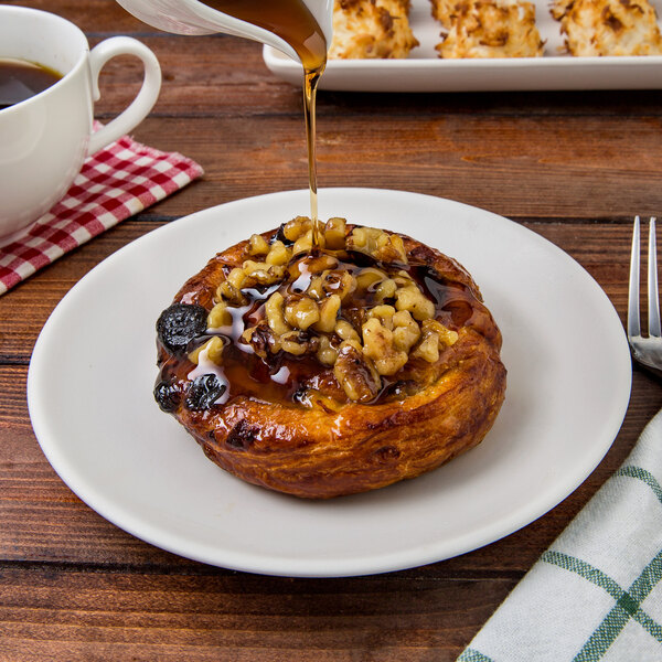 A TuxTrendz Zion matte white coupe china bread and butter plate with a pastry and nuts and syrup on it.