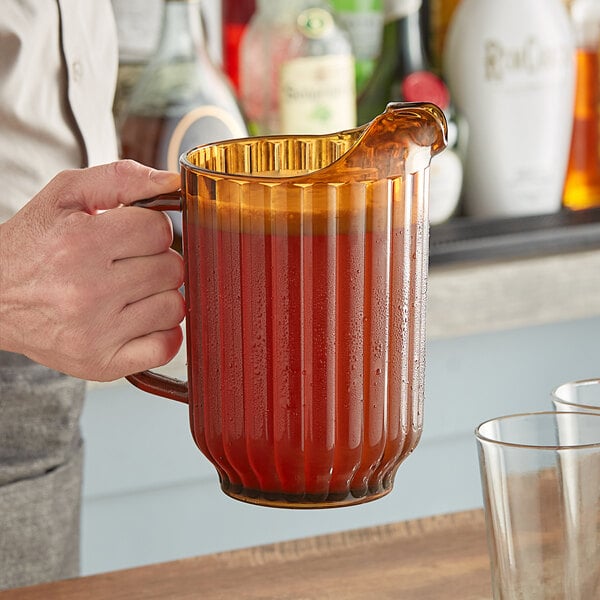 A man pouring liquid from a Cambro Amber plastic pitcher into a glass with a straw.