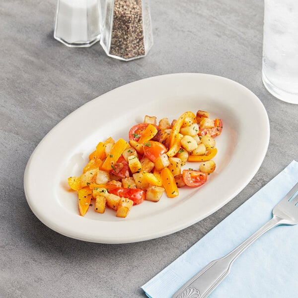 An Acopa ivory stoneware platter with a fork and knife on a napkin next to a plate of food.