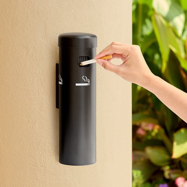 A black wall-mounted cigarette receptacle with a person disposing of a cigarette.
