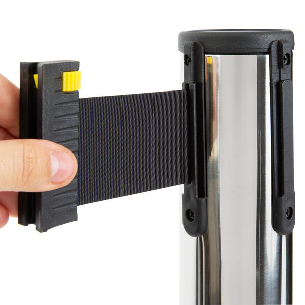A hand attaching a black and yellow sign holder to a silver Lancaster Table & Seating crowd control stanchion pole.