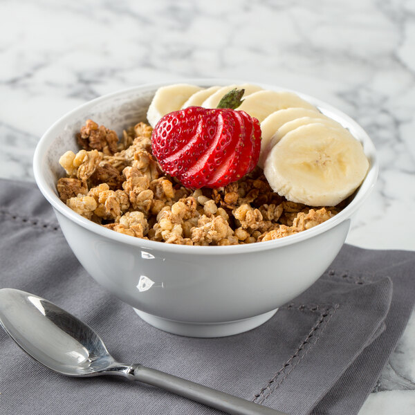 A Schonwald round porcelain bowl filled with cereal and fruit with a spoon next to it.