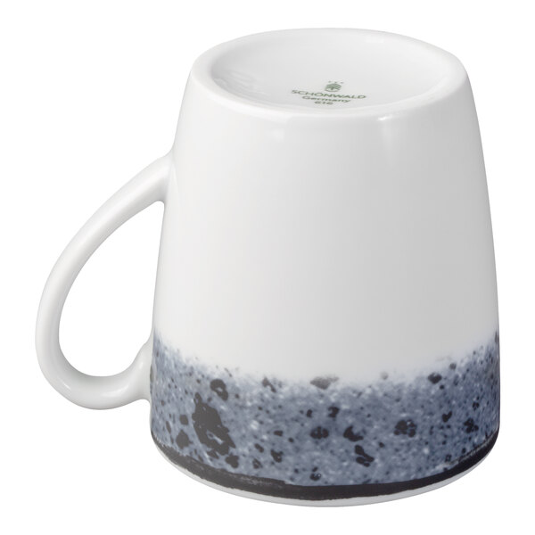 A white porcelain cup with a handle, shown upside down, featuring a speckled blue and black pattern around the base.