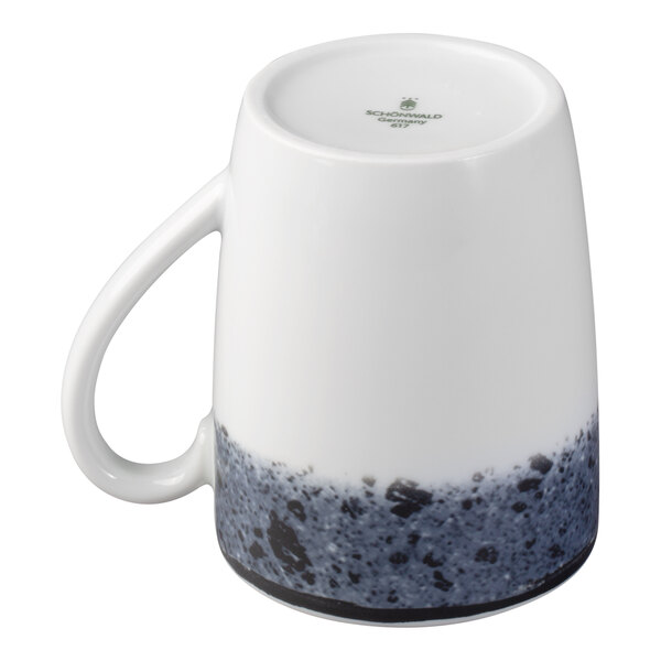 A white porcelain mug with a handle, featuring a speckled blue and black pattern around the base, shown upside down.