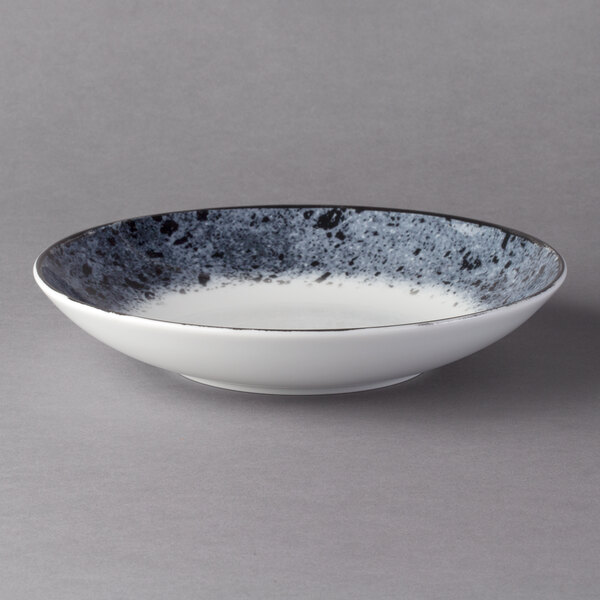 A white porcelain deep coupe plate with a black speckled rim.