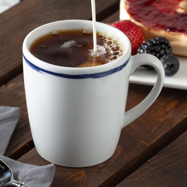 A Schonwald dark blue porcelain tall cup with coffee and a pastry on a table.