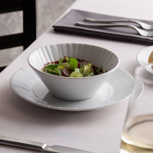 A white Schonwald porcelain bowl filled with salad on a table.