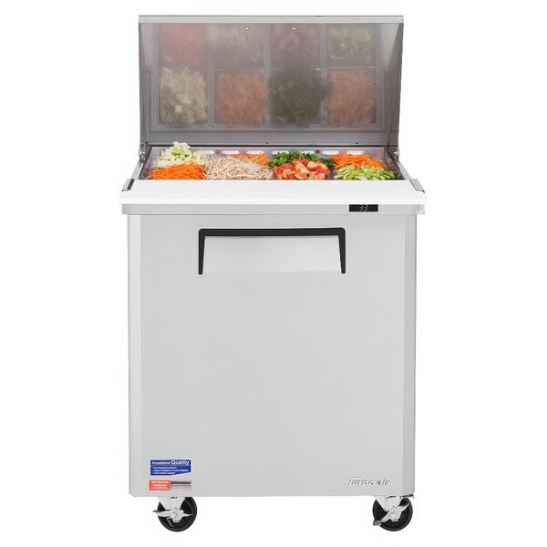 A Turbo Air refrigerated sandwich prep table with a stainless steel top and wheels filled with containers of vegetables.