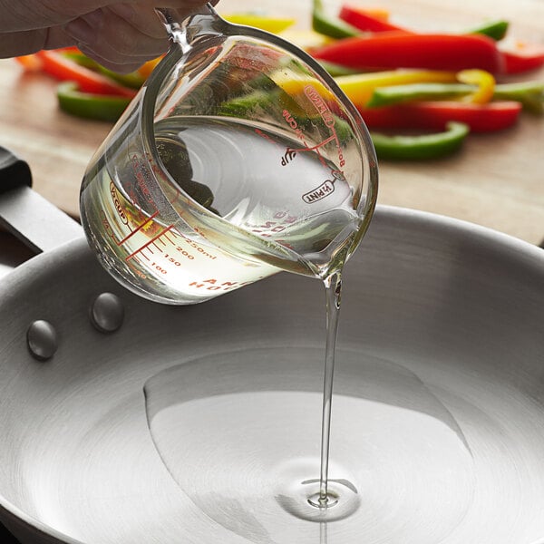 A hand pouring Admiration 100% Pure Vegetable Oil into a pan of vegetables.