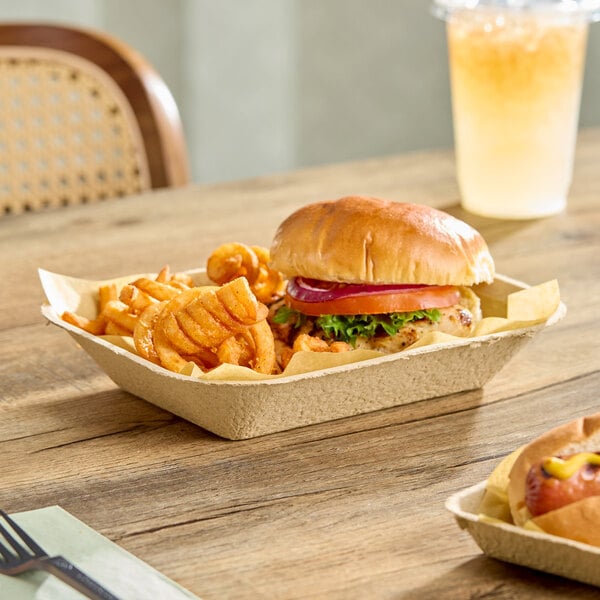 A rectangular molded fiber tray containing a sandwich and curly fries on a wooden table.