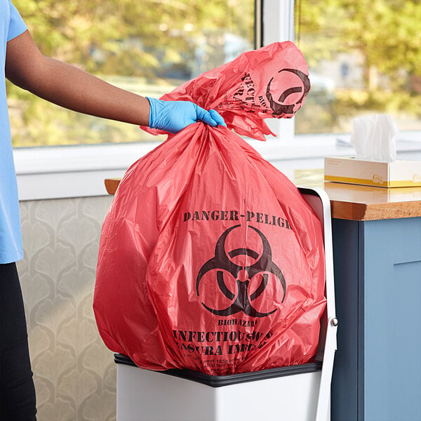 A hand in a blue glove holding a red biohazard bag.