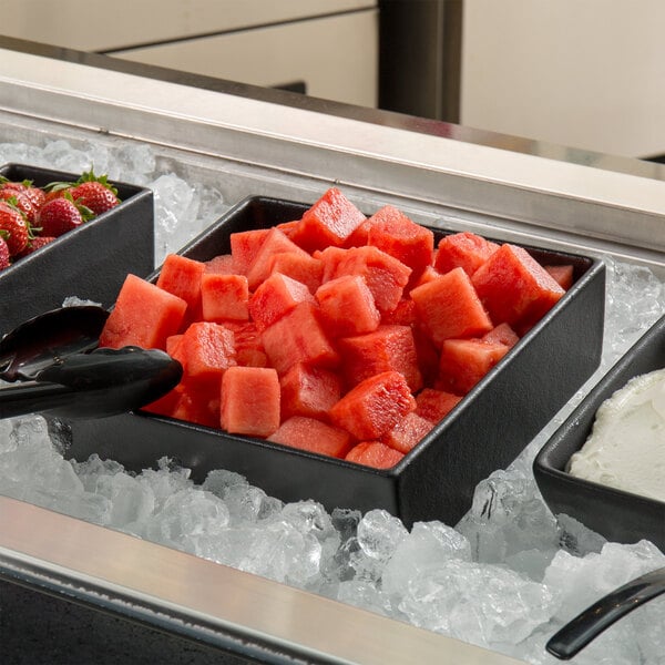 A G.E.T. Enterprises Bugambilia black resin-coated square salad bowl filled with watermelon cubes on ice.