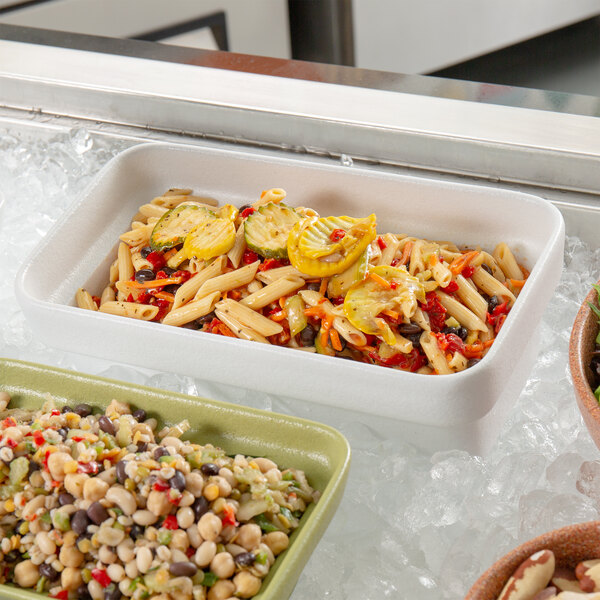 A white rectangular china bowl filled with pasta and vegetables on a green tray on a counter in a salad bar.