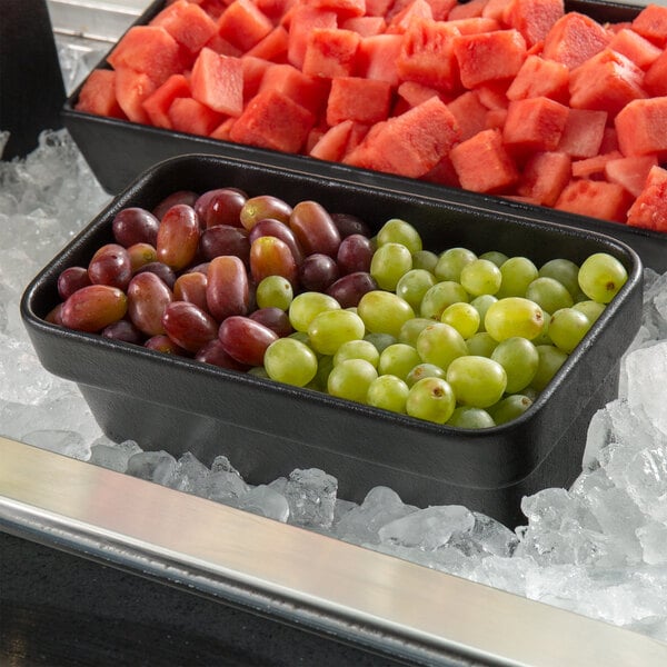 A black G.E.T. Enterprises Bugambilia rectangular china bowl filled with grapes and watermelon.