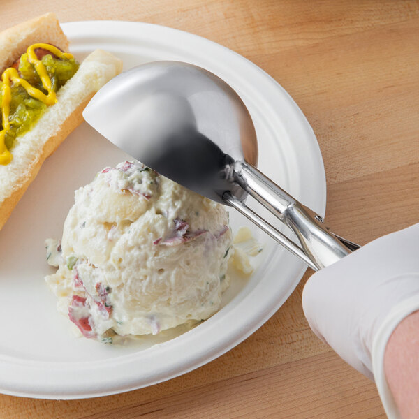 A person using a Vollrath stainless steel squeeze handle disher to scoop potato salad onto a plate of food.