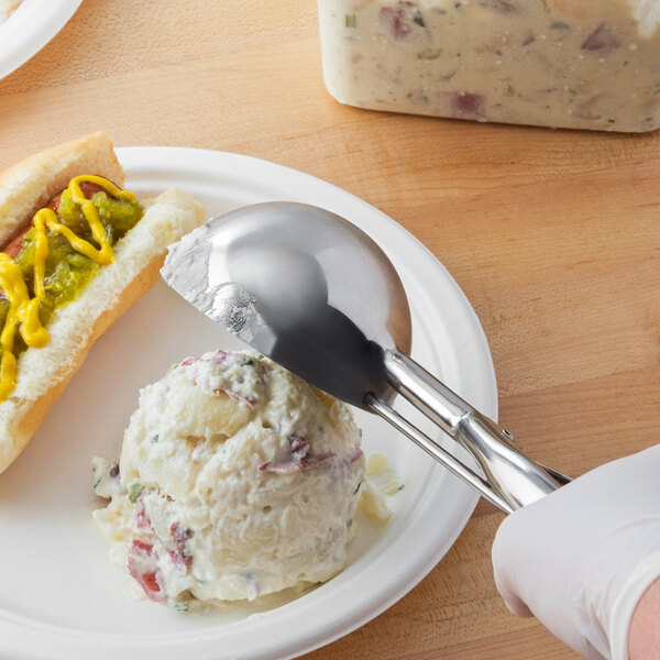 A gloved hand uses a Vollrath #6 stainless steel disher to scoop ice cream onto a plate of food.