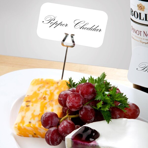 A plate of cheese and grapes with Ateco label holders on a table.