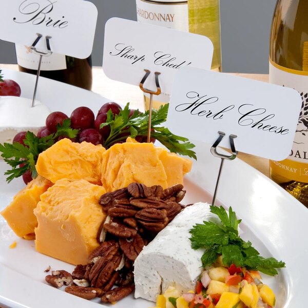 A white plate with cheese, fruit, and a label holder with a name on it.