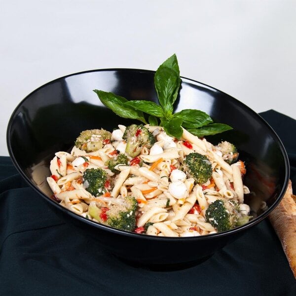 A black slanted melamine bowl filled with pasta, broccoli, and basil.