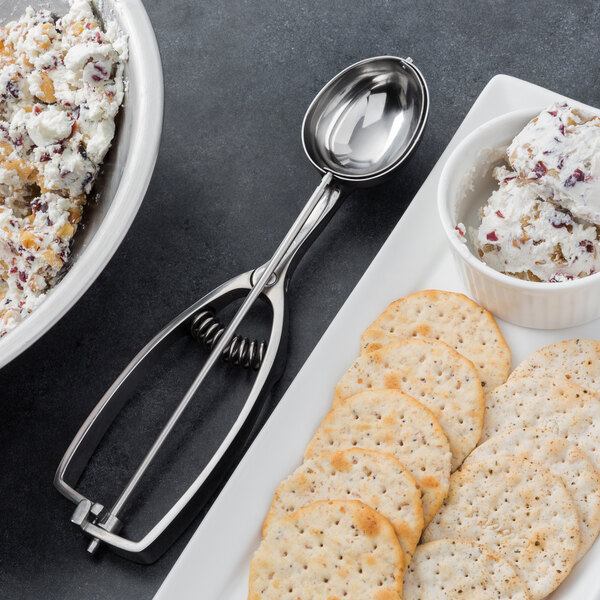 A Vollrath stainless steel oval disher with food in a bowl and a spoon.
