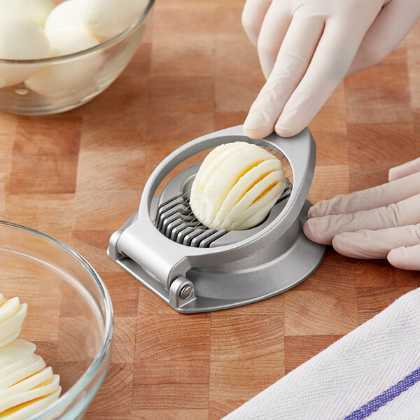 A gloved hand uses a Vollrath egg slicer to slice a white egg.