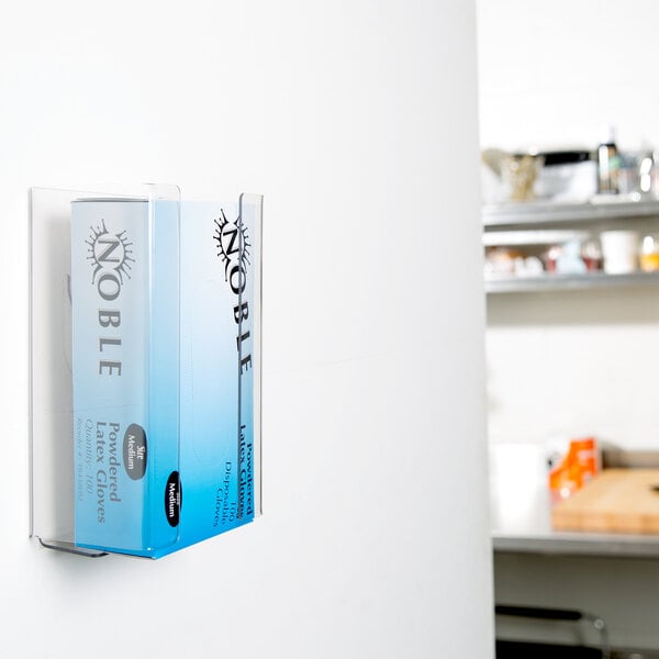 A San Jamar clear plexiglas wall-mounted disposable glove dispenser.