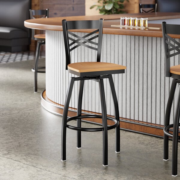 A black metal bar stool with a cross back design and a natural wood seat.