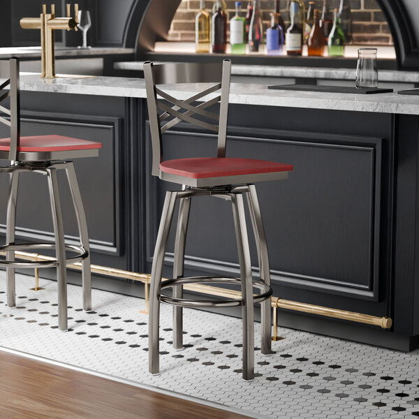 A metal bar stool with a cross back design, swivel feature, and a mahogany wood seat.