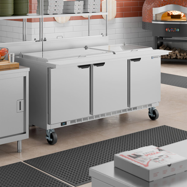 A large stainless steel, three-door mega top refrigerated sandwich prep table on wheels.