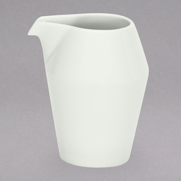 A Schonwald white porcelain creamer with a handle on a gray surface.