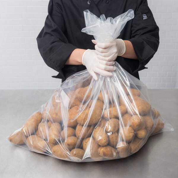 A person in a chef's uniform wearing gloves holding a LK Packaging heavy-duty plastic food bag full of potatoes.