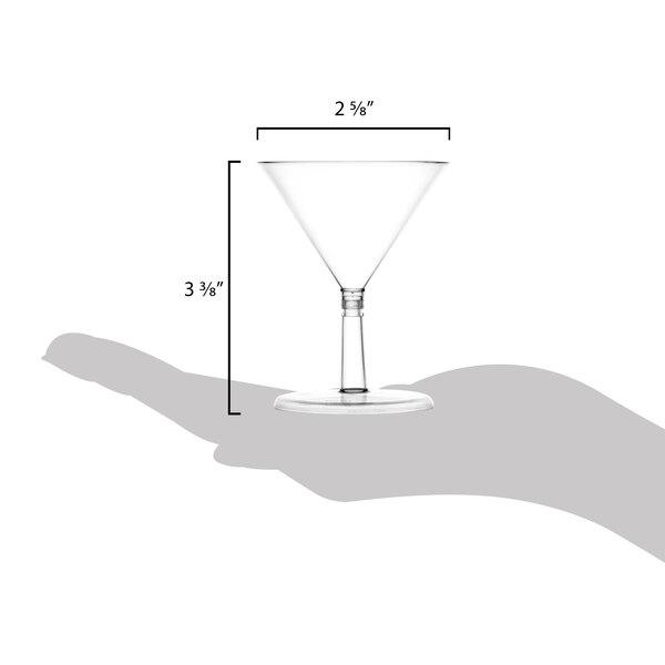A hand holds a clear WNA Comet 2 oz. plastic martini glass with measurements.