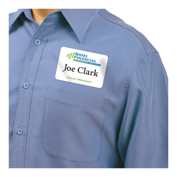A person wearing a blue button-up shirt with a rectangular adhesive name badge on the chest.